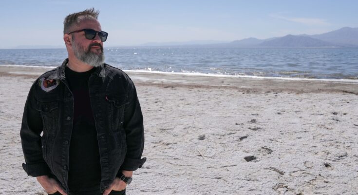 Matt Pryor standing in beach sand wearing all black.