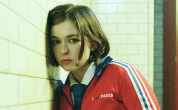 Snail Mail leaning on a subway tile wall.