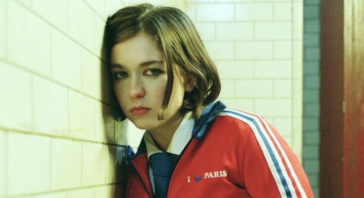 Snail Mail leaning on a subway tile wall.